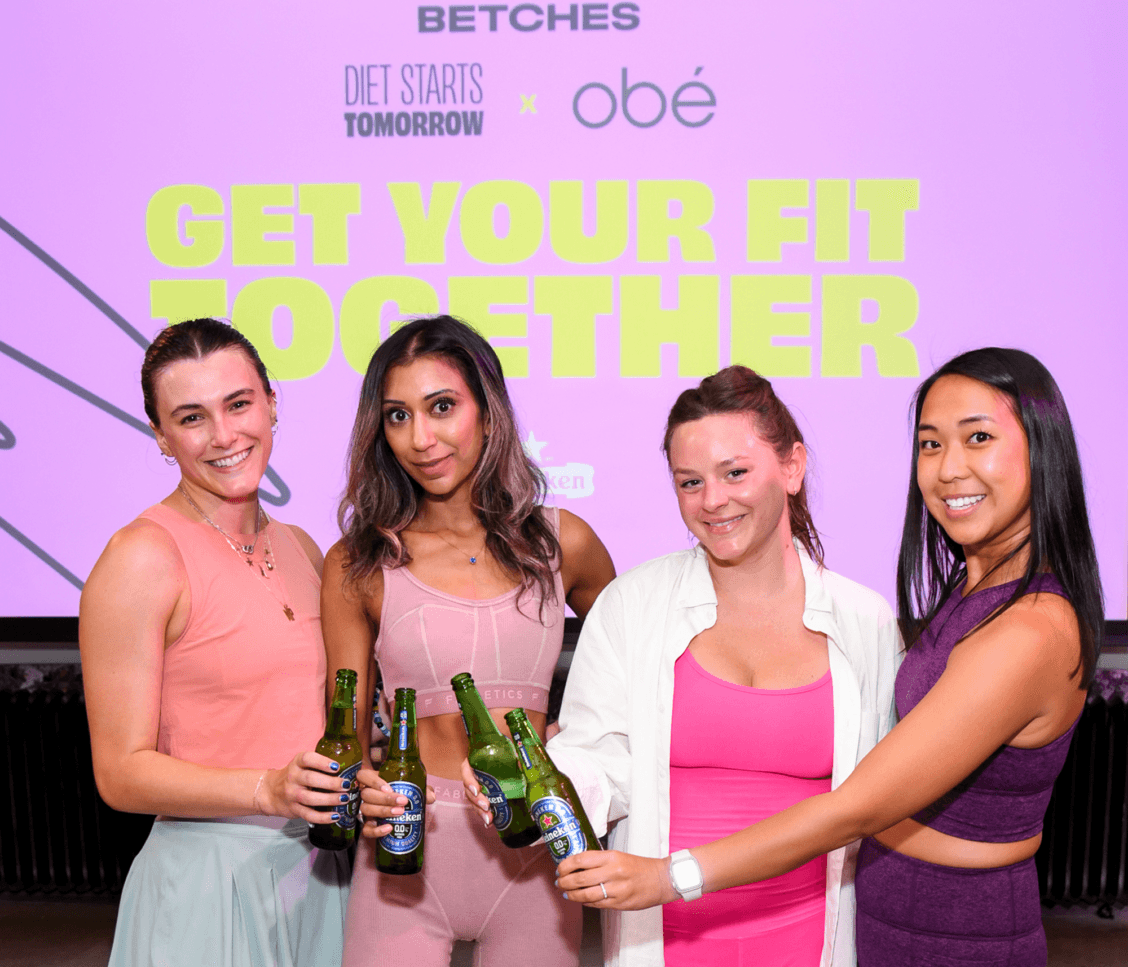 Four members of the Betches team holding bottles of beer, making a "cheers" gesture